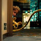 Ein Notausgangsschild mit Pfeil nach rechts. Ein Junge und ein Tier mit gelbem Fell und großen Augen schauen um die Ecke.