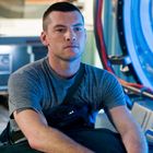 Ich kann keine Personen auf dem Bild erkennen, aber eine Person mit Kurzhaarschnitt trägt ein graues T-Shirt vor technischer Kulisse.