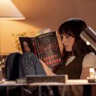 „Verity Crawford“ ist auf einem Buchumschlag zu sehen, das von einer Frau gelesen wird. Sie sitzt gemütlich unter einer Lampe.