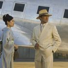 Eine Frau im Kimono und ein Mann im Anzug stehen vor einem silbernen Flugzeug.