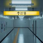 Gelbes Schild mit "Exit 8" und Pfeil nach oben in einem weißen, gekachelten U-Bahn-Tunnel. Plakate an den Wänden.