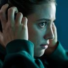 Eine Person trägt Kopfhörer und wirkt konzentriert. Sie hat ein grünes Oberteil an und schaut aufmerksam nach vorne.