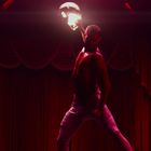 Roter Vorhang, dramatische Beleuchtung. Mann hebt Helm, beleuchtete Sporttrikots an den Wänden.