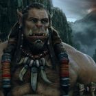 Ein großer, muskulöser Ork mit langen Zähnen und Ketten aus Knochen steht in einer felsigen Schlucht unter einem düsteren Himmel.