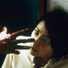 Eine verängstigte Frau schaut auf eine blutige Hand, die sich ihr nähert.