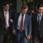 Drei junge Männer in Anzügen laufen nebeneinander; sie tragen Krawatten und Rucksäcke.