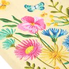 Bestickte Blumen in leuchtenden Farben, darunter ein rosa, ein blaues und ein gelbes Blütenmotiv, mit Schmetterlingen.