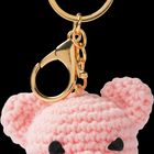 Ein gehäkelter Schlüsselanhänger in Form eines rosa Schweins mit goldfarbenem Ring und Karabiner.