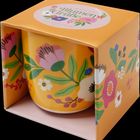 Auf der Verpackung steht "Bunte Blumengrüße", sie enthält einen gelben Becher mit buntem Blumenmuster.
