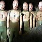 Zahlen 32, 27, 3, 47 auf Vorderseite von Anzügen. Mehrere humanoide Figuren in futuristischen Anzügen in einer Höhle.