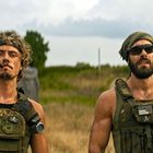 Zwei Männer in militärischer Ausrüstung. Texte auf der Weste: „Raining Freedom“ und Totenkopf-Symbole.