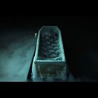 Ein Sarg, bedeckt mit einem Spitzentuch, schwebt in Nebel, eine brennende Kerze daneben.