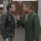 Zwei Männer streiten sich heftig in einem Hof. Einer trägt eine Lederjacke, der andere einen grünen Mantel. Passanten im Hintergrund.