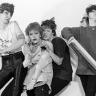 Eine Gruppe von vier Menschen posiert mit Gegenständen. Eine Person trägt ein Shirt mit der Aufschrift "mad in".