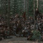 Viele Menschen in einem Wald, einige bewaffnet, konzentriert und in Uniformen, einige halten eine rote Fahne.