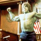 Eine grüne, muskulöse Figur brüllt in einem Gerichtssaal, Arme erhoben, mit US-Flaggen im Hintergrund.