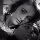 Eine Frau stützt ihren Kopf auf den Arm eines schlafenden Mannes, beide wirken entspannt und nahe. Szenerie in Schwarzweiß.