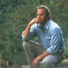 Ich kann den Text nicht erkennen. Ein Mann in blauer Kleidung hockt nachdenklich im Grünen, umgeben von Natur.