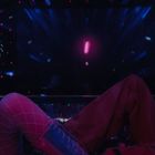 Zwei Personen in einer dunklen Umgebung mit bunten Lichtern, eine trinkt aus einem Glas, die andere lächelt.