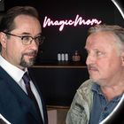 "MagicMom" in Leuchtschrift. Zwei Männer stehen sich gegenüber, umgeben von einem runden Licht.
