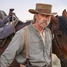 Ich kann die Person nicht identifizieren. Ein älterer Mann mit Schnurrbart und Cowboy-Hut steht neben zwei Pferden.