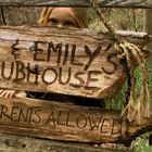 „Jack & Emily's Clubhouse, No Parents Allowed“. Ein Kind schaut durch ein rustikales Holztor mit Schildern.