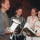 Eine Gruppe von vier Personen interagiert fröhlich. Einer hält einen Wasserkocher, eine andere ein Buch.
