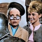 Zwei Frauen schauen lächelnd auf eine Ritterrüstung. Eine trägt Brille und Hut, die andere hat eine elegante Hochsteckfrisur.