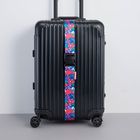 Text: BEIS. Schwarzer Rollkoffer mit blauem, blumenbedrucktem Gurt. Koffer hat vier Rollen und gerippte Oberfläche.