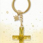 „Dein Wegbegleiter“. Goldener Schlüsselanhänger mit Kreuz und Sternanhänger auf gelbem, sternenbesetztem Hintergrund.