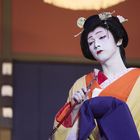 Eine Person in traditioneller japanischer Kleidung mit weiß geschminktem Gesicht.