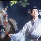 Eine Person in traditioneller Kleidung hält ein Pferd am Zügel.