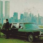 Zwei Männer stehen neben einer Limousine. Im Hintergrund sieht man eine Skyline mit zwei hohen Türmen.