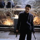 Ein Mann im Anzug steht vor einer Wand mit Reliefs und Figurinen, die in Vitrinen ausgestellt sind.