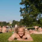 Ich sehe keinen Text. Eine Person liegt lächelnd auf einer Wiese, umgeben von mehreren Menschen im Park.