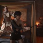 Ich kenne den Text nicht. Eine Frau in schwarzer Kleidung hält eine Peitsche; ein Mann dahinter mit kimonoähnlicher Kleidung und Pistole.