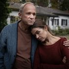 Ich kann keine Personen identifizieren. Eine Frau lehnt an der Schulter eines Mannes. Ein Haus ist im Hintergrund zu sehen.