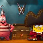 Zwei Comicfiguren in Piratenkostümen stehen vor einer Schatzkiste. Im Hintergrund sind gekreuzte Schwerter sichtbar.