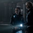 Zwei Personen in dunkler, futuristischer Kleidung mit Taschenlampen in einer düsteren, säulengestützten Umgebung.