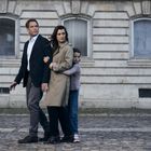 Ein Mann, eine Frau und ein Mädchen gehen auf Kopfsteinpflaster vor einem alten Gebäude. Das Mädchen hält die Frau fest.