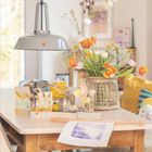 April 2027 Kalenderblatt. Frühlingshafte Tischdekoration mit Blumenstrauß und Papierdekorationen. Helles Interieur.