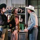 Text: "OVERLAND HOTEL." Drei Männer in Westernkleidung, zwei tragen Hüte, einer zieht eine Waffe auf einen anderen.