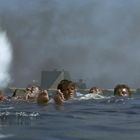 Ich kann keine spezifischen Texte im Bild erkennen. Eine Gruppe Menschen schwimmt im Wasser, während eine Wasserfontäne aufsteigt.