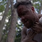 Zwei Personen sind in einem dichten Wald, eine hält die andere aggressiv am Kragen fest.