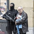 Texte: "Boikota frantses produktuak". Ein Mann hält eine Katze, daneben ein Polizist in schwarzer Uniform mit Waffen.