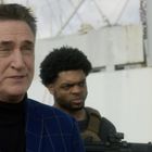 Zwei Männer stehen vor einem grauen Schiff. Der vordere trägt ein blaues Karo-Jackett, der hintere eine Schutzweste.