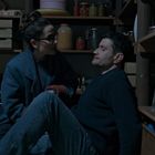 Ein Mann sitzt mit geschlossenen Augen auf einem Boden. Links ein Kind in Jacke, rechts das unscharfe Gesicht einer Frau.