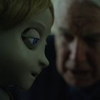 Eine ältere Person schaut ein Kind mit puppenhaftem Gesicht und blauen Augen intensiv an.