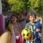 Kinder in bunten Badeanzügen, mit Schwimmutensilien und einem Fußball, stehen fröhlich im Eingang.