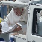 Ein weiß gekleideter Mann beugt sich lächelnd aus einem Fahrzeug, um mit einem Kind im blauen Kostüm zu interagieren.